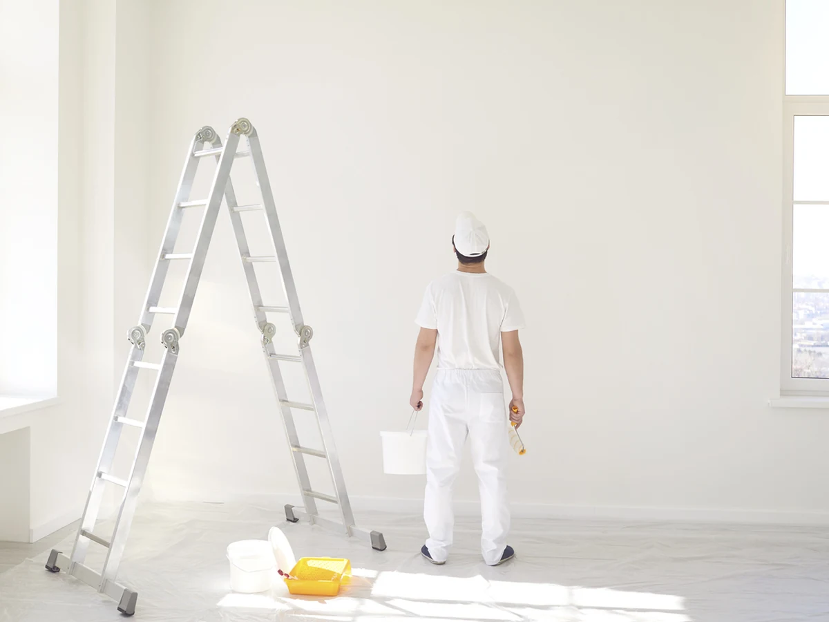 Painter on a white ladder working on upper wall surfaces in a Cambridge property